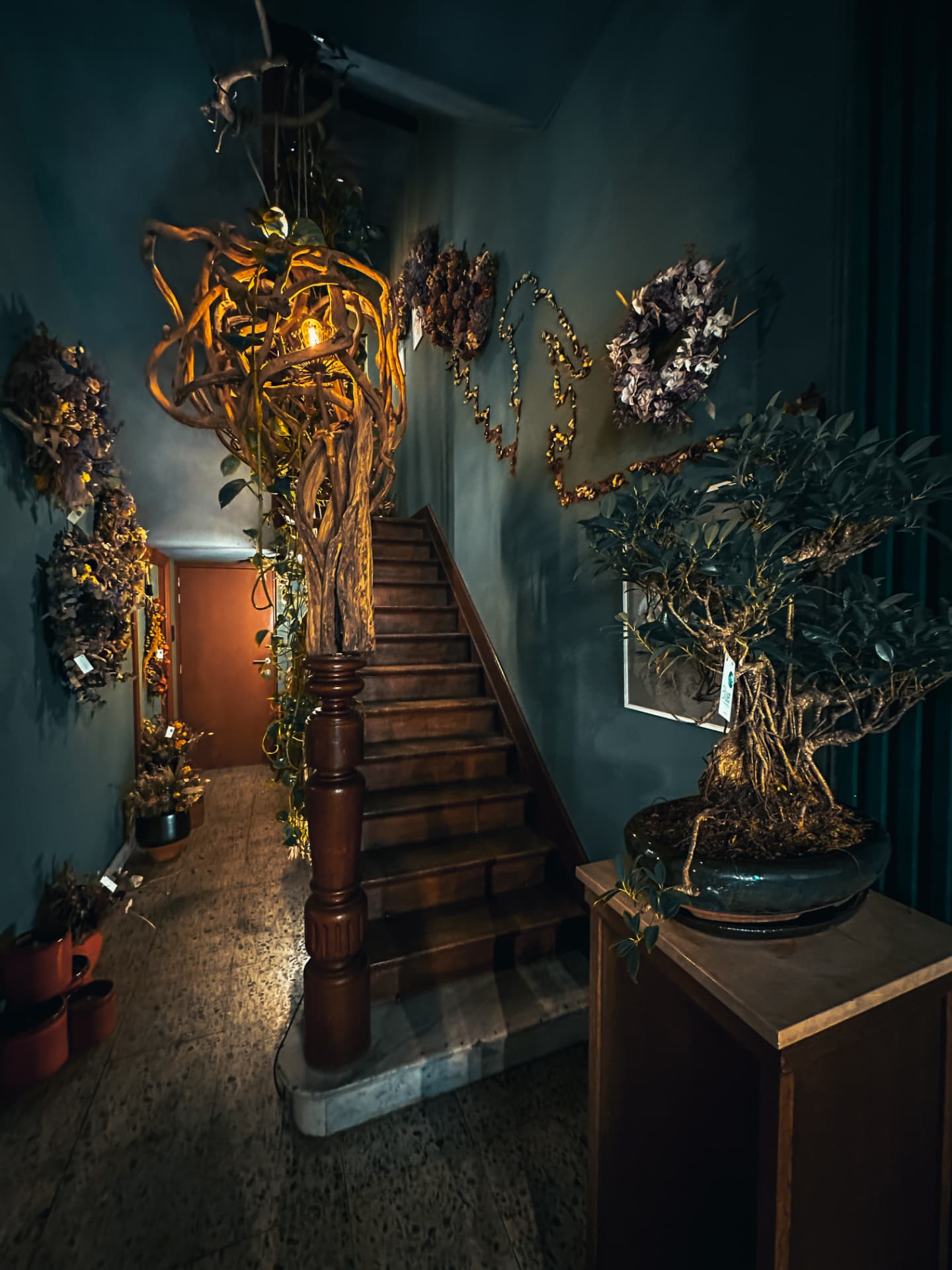 Dimly lit boutique staircase framed by dried floral wreaths and a bonsai tree